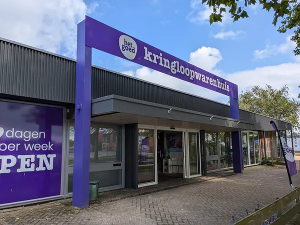 Paarse gevel van kringloopwinkel Het Goed met grote naam boven ingang, winkelramen en deuren zichtbaar