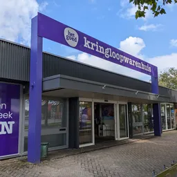 Paarse gevel van kringloopwinkel Het Goed met grote naam boven ingang, winkelramen en deuren zichtbaar