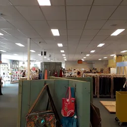 Overzicht van de winkelvloer met kledingrekken, tassen en diverse tweedehands artikelen onder fluorescente verlichting