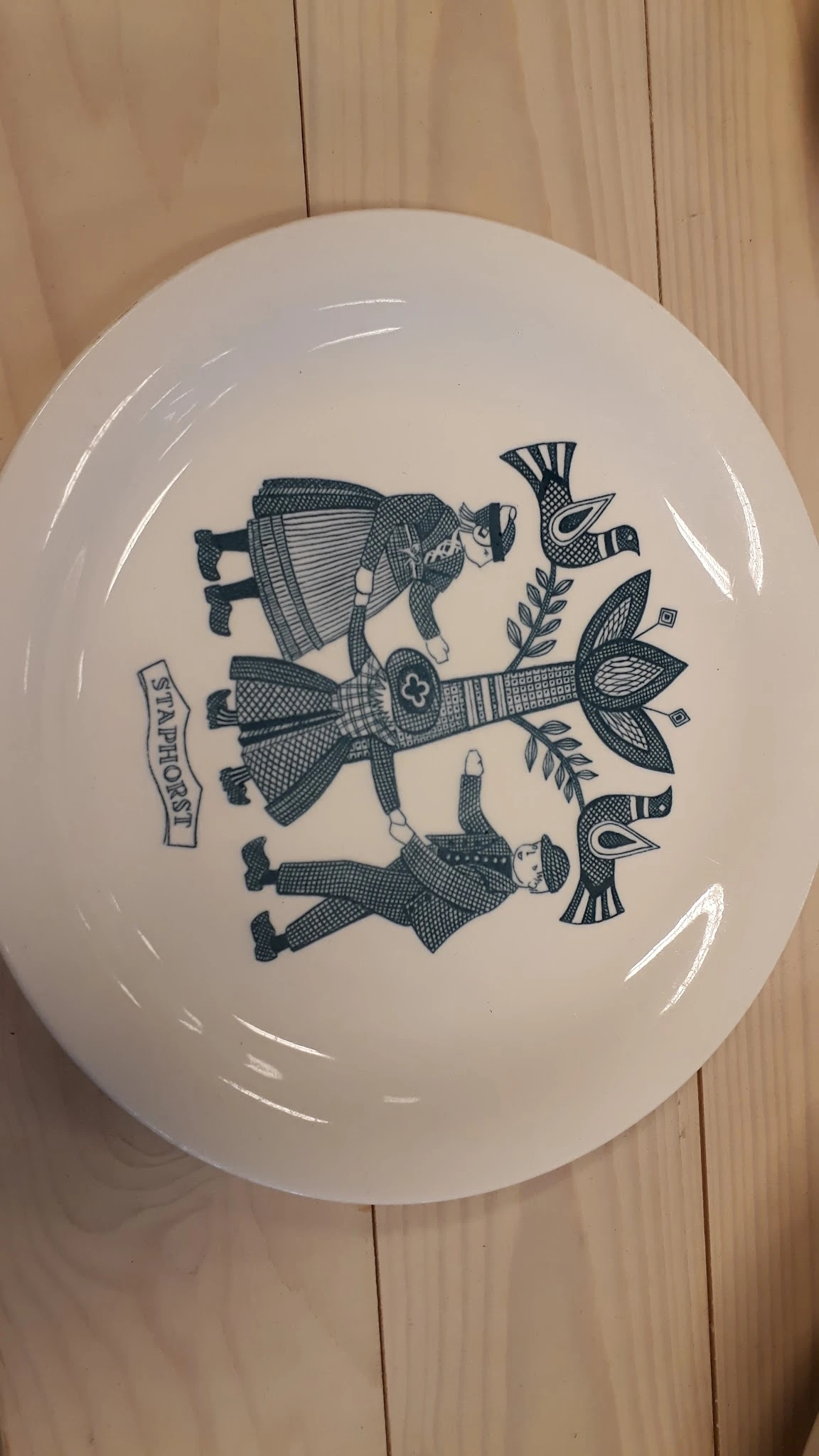 Wit serviesbord met donkerblauwe decoratieve tekening van drie figuren in traditionele kledij en bloemmotieven