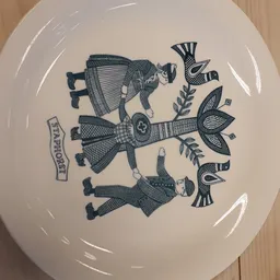 Wit serviesbord met donkerblauwe decoratieve tekening van drie figuren in traditionele kledij en bloemmotieven