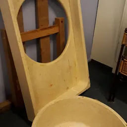 Geel kunststof stoel met gat in de rugleuning, tegen houten frame