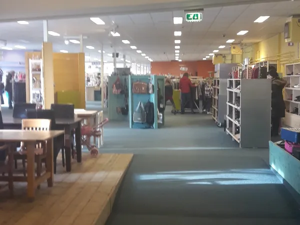Winkelvloer van kringloopwinkel met stellingen, kleding aan hangers en verschillende afdelingen met gekleurde wanden