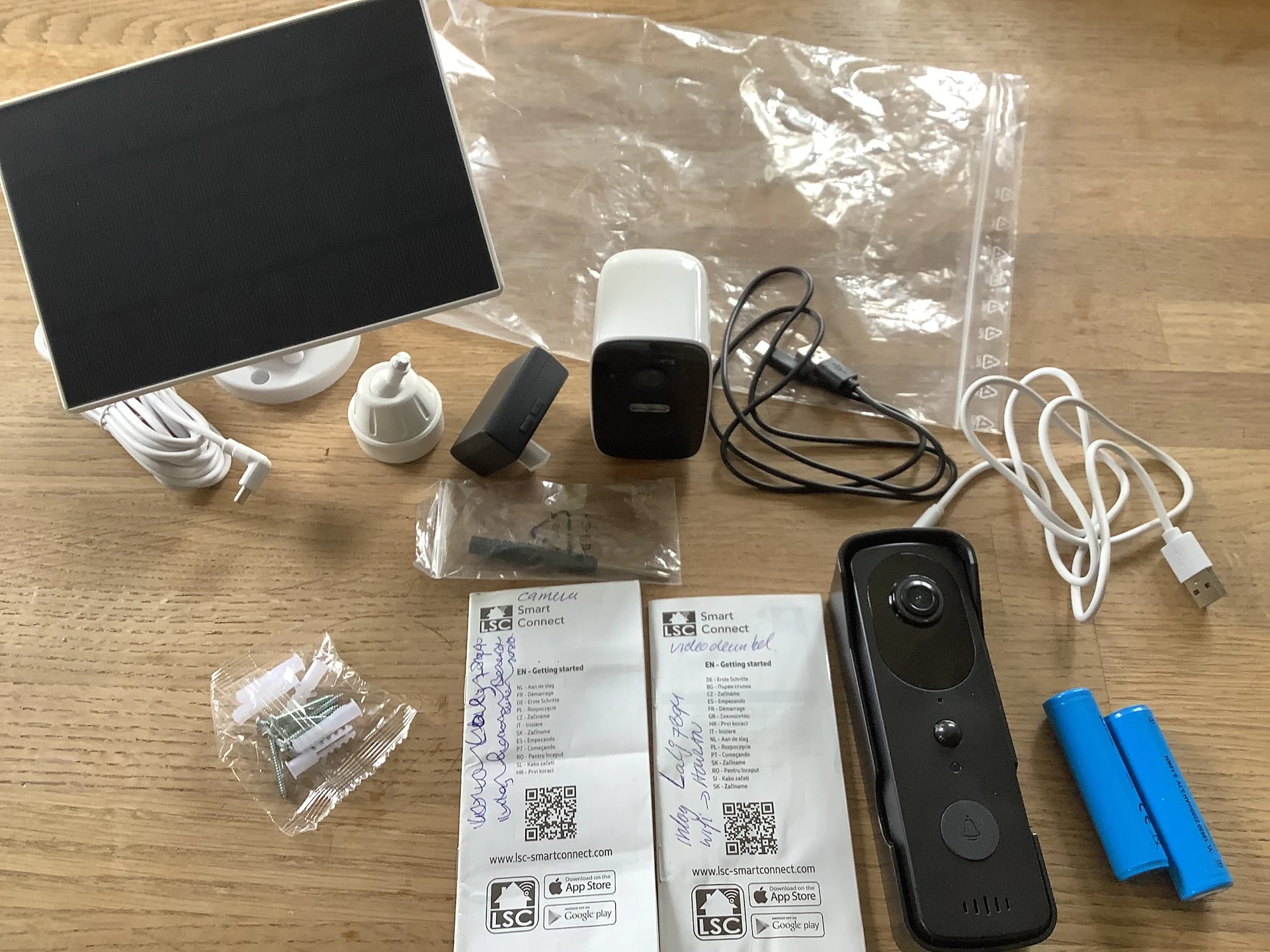 Uitpakking van beveiligingscamera set met witte hub, zwarte videodeurbel, kabels, batterijen en handleidingen