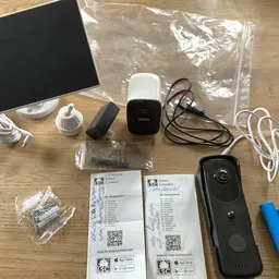 Uitpakking van beveiligingscamera set met witte hub, zwarte videodeurbel, kabels, batterijen en handleidingen