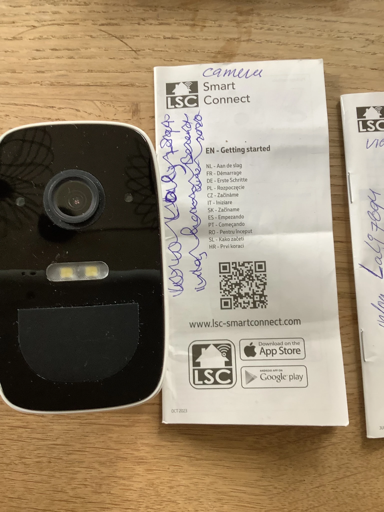 Zwarte videodeurbel met camera en instructiekaart met meertalige handleiding