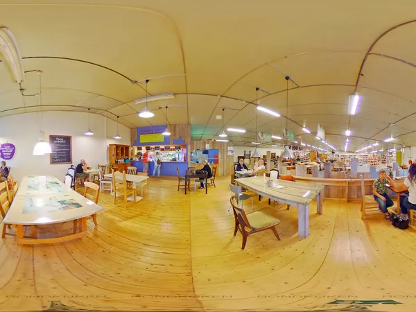 Ruim interieur van kringloopwarenhuis met houten vloer, tafels, stoelen en diverse kasten verspreid over het verkoop­oppervla