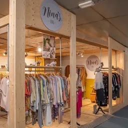 Winkelinterieur met houten stellingen vol opgehangen kleding, winkelcircels aan het plafond, moderne verlichting en open ruim