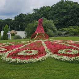 Bloemenperk met rode en witte bloemen in een park, met een topiary-sculptuur op de achtergrond