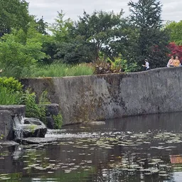 Waterpartij met betonnen wand en groene bomen, mensen op achtergrond