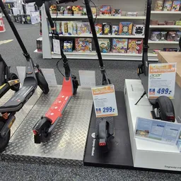 Uitstalling van elektrische stepjes en scooters met prijskaartjes in een kringloopwinkel