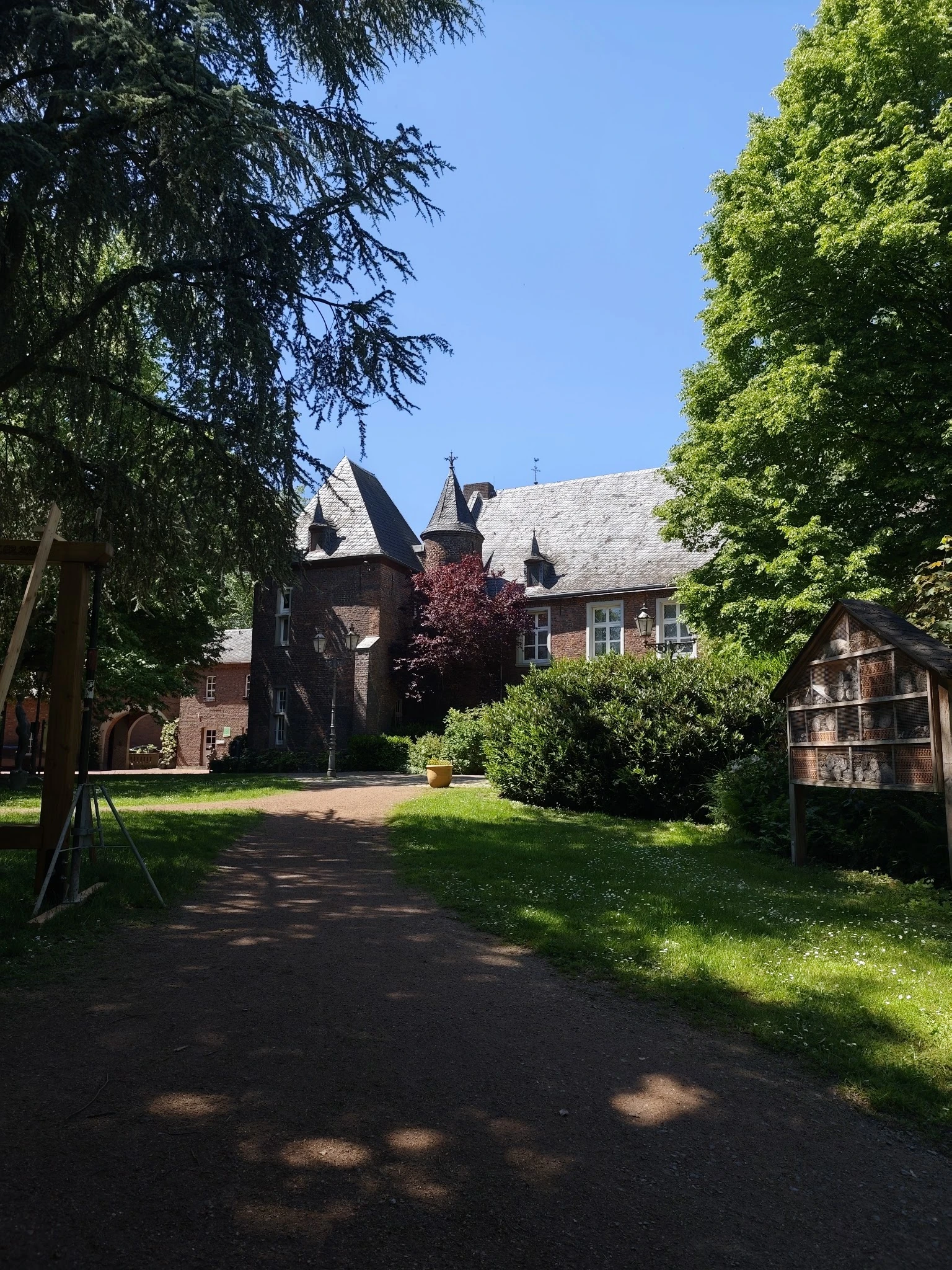 Bakstenen kringloopwinkel met torentjes omgeven door groene struiken en bomen