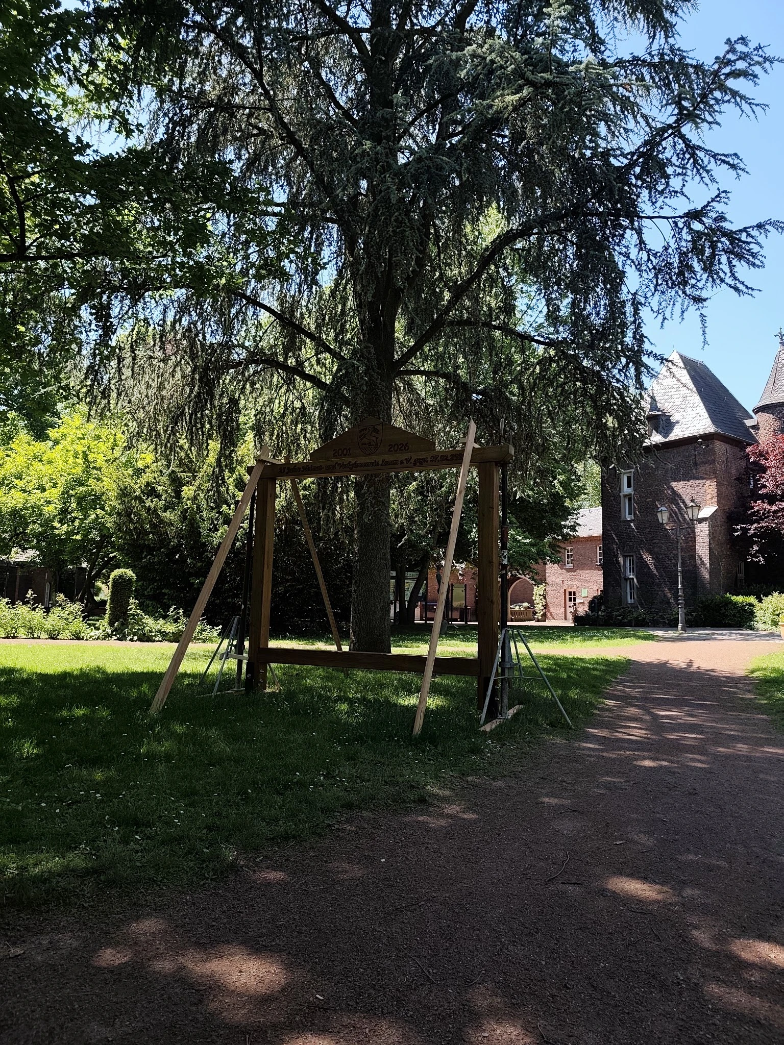 Bakstenen gebouw met toren achter een houten schommel onder een wilg in een park
