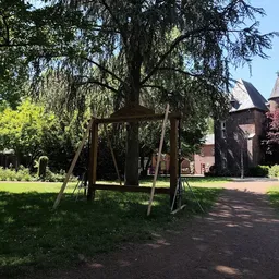Bakstenen gebouw met toren achter een houten schommel onder een wilg in een park