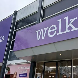 Paarse gevel van kringloopwinkel met 'welko' zichtbaar en glazen deuren