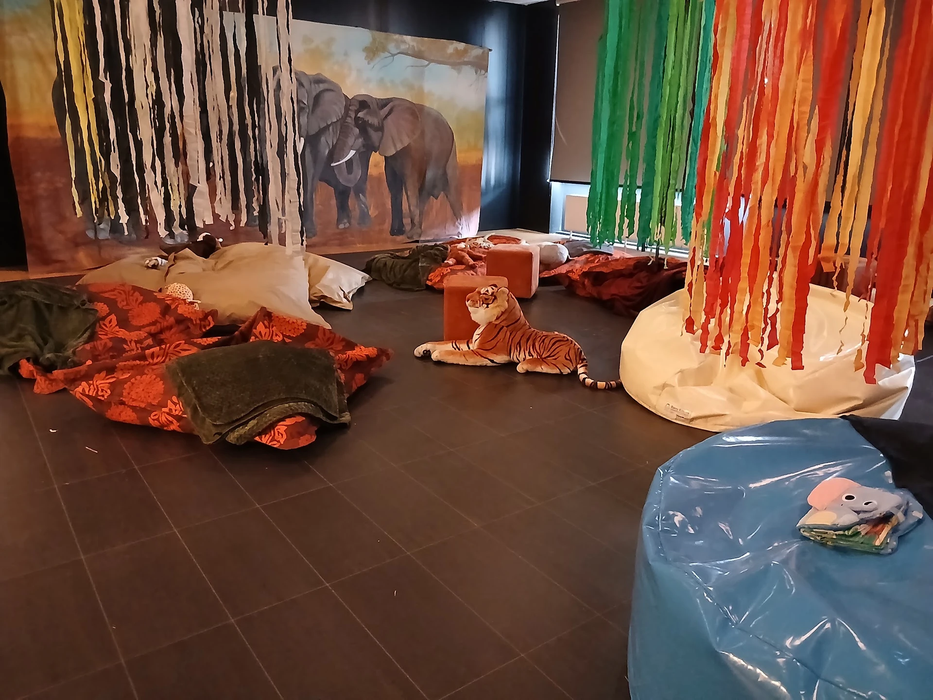 Winkelinterieur met thema-decoratie: speelgoedtapijten, sjaals aan rek, schilderij met olifant, diverse voorwerpen op donkere