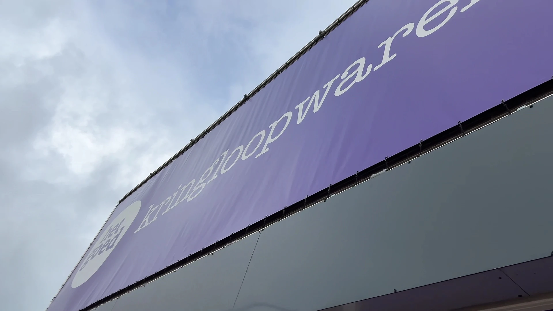 Paarse gevel van kringloopwarenhuis met witte tekst en logo