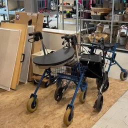 Blauwe rollator met zwart zitje en winkelmandje, op een kurken ondergrond in de winkel