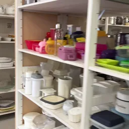 Kastplanken met huishoudartikelen: servies, bakjes, bewaardozen en keukengerei in verschillende kleuren