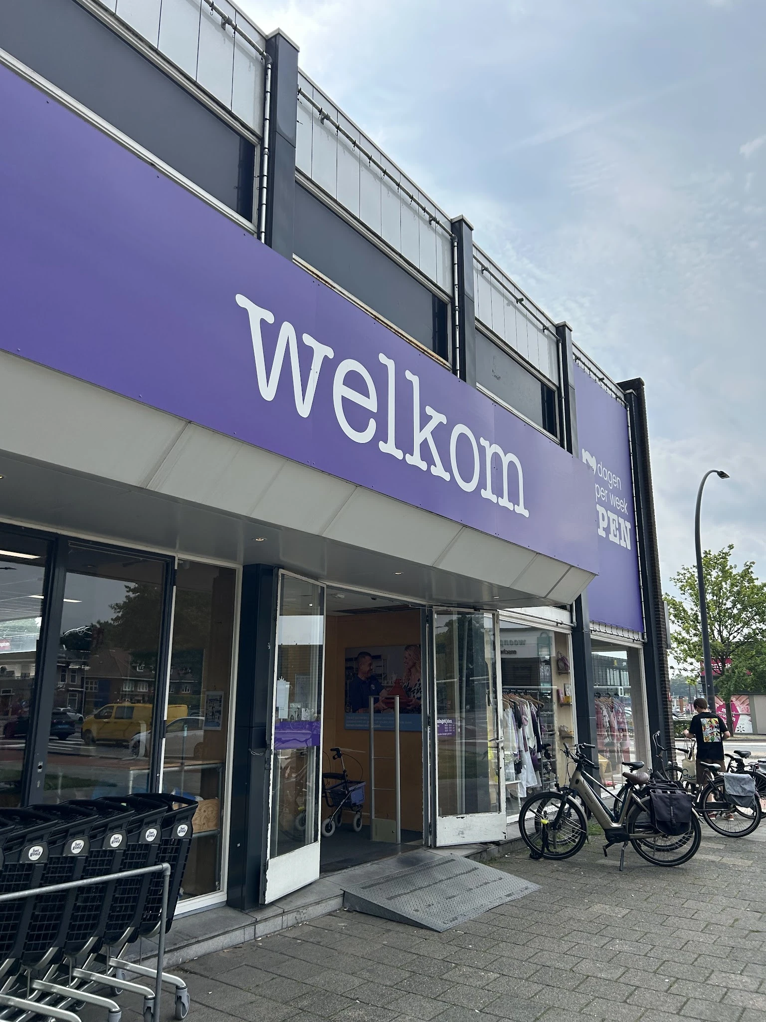 Paarse gevel van kringloopwinkel met grote ramen en winkelnaam 'Welkom' in witte letters