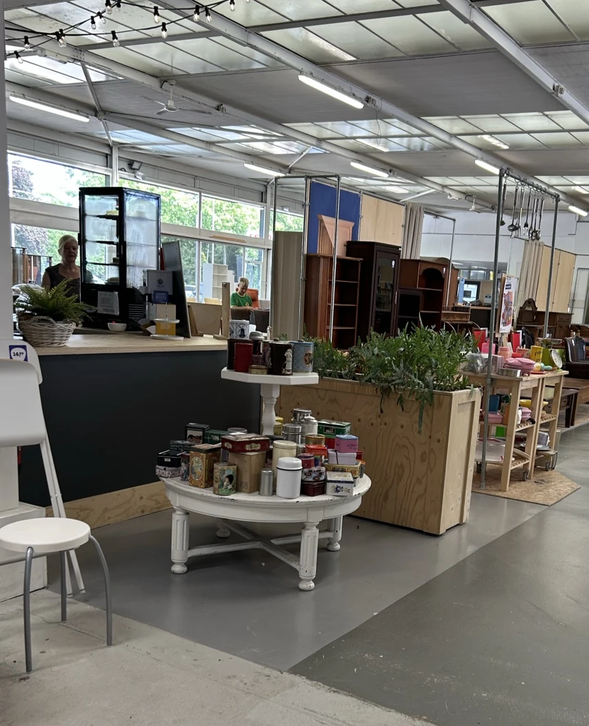 Winkelinterieur met witte ronde toonbank met potjes en een plantenbak, houten stellingen en kasten op de achtergrond
