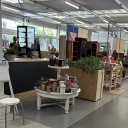 Winkelinterieur met witte ronde toonbank met potjes en een plantenbak, houten stellingen en kasten op de achtergrond
