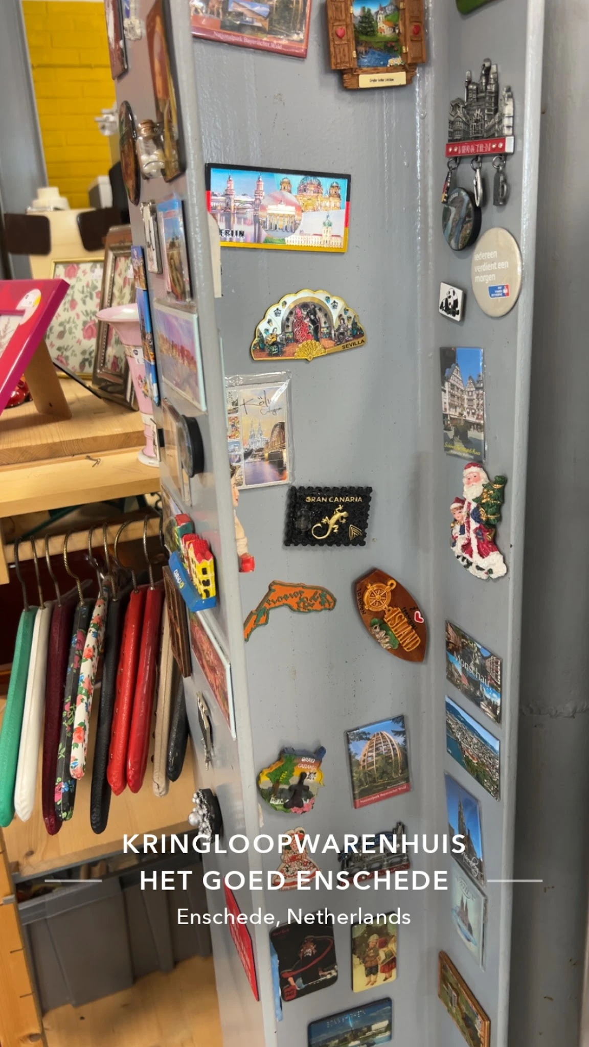 Wand met diverse souvenirs en reisherinneringen, waaronder magneten, ansichtkaarten en decoratieve items