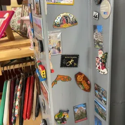 Wand met diverse souvenirs en reisherinneringen, waaronder magneten, ansichtkaarten en decoratieve items