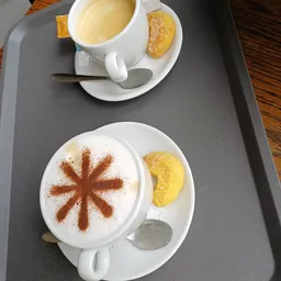Twee kopjes cappuccino met kaneeldecoratie en beschuit op grijze tafel in lunchroom
