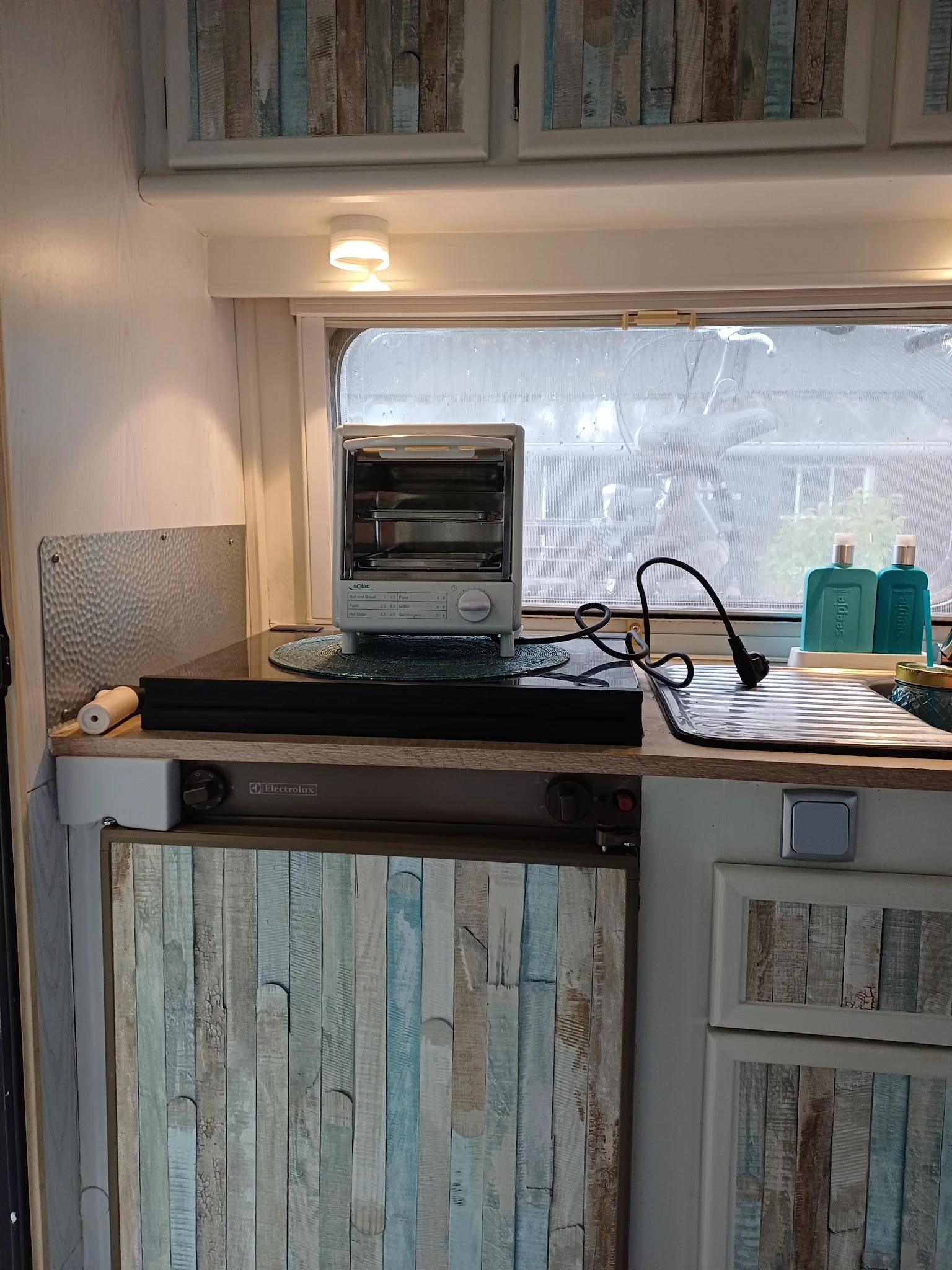 Tafelmodel elektrische oven op een zwart onderstel met stopcontact en toiletartikelen op het werkblad