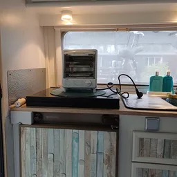 Tafelmodel elektrische oven op een zwart onderstel met stopcontact en toiletartikelen op het werkblad