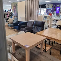 Winkelinterieur met houten tafels, zwarte en blauwe fauteuils, stellingen en gordijnen in een kringloopwinkel