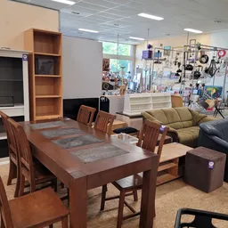 Winkelinterieur met houten eettafel, stoelen, groen zitmeubel en wanddisplay met diverse huishoudartikelen