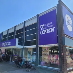 Hoekpand met paarse en witte gevelbekleding, grote ramen met etalages, fietsen geparkeerd voor de ingang, banner 'OPEN' zicht