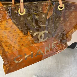 Close-up van een doorzichtige tas of accessoire met Chanel CC-logo en oranje details
