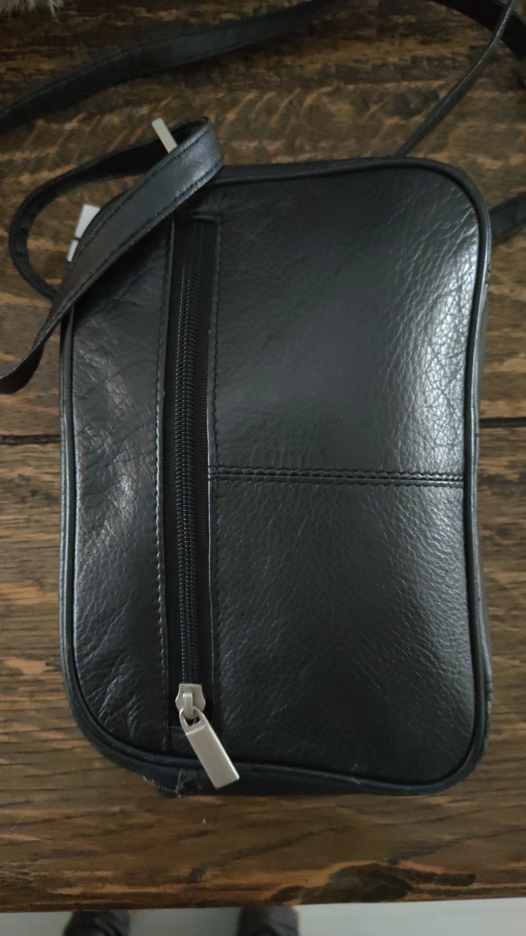Zwarte lederen clutch of kleine handtas met ritssluiting, op houten ondergrond