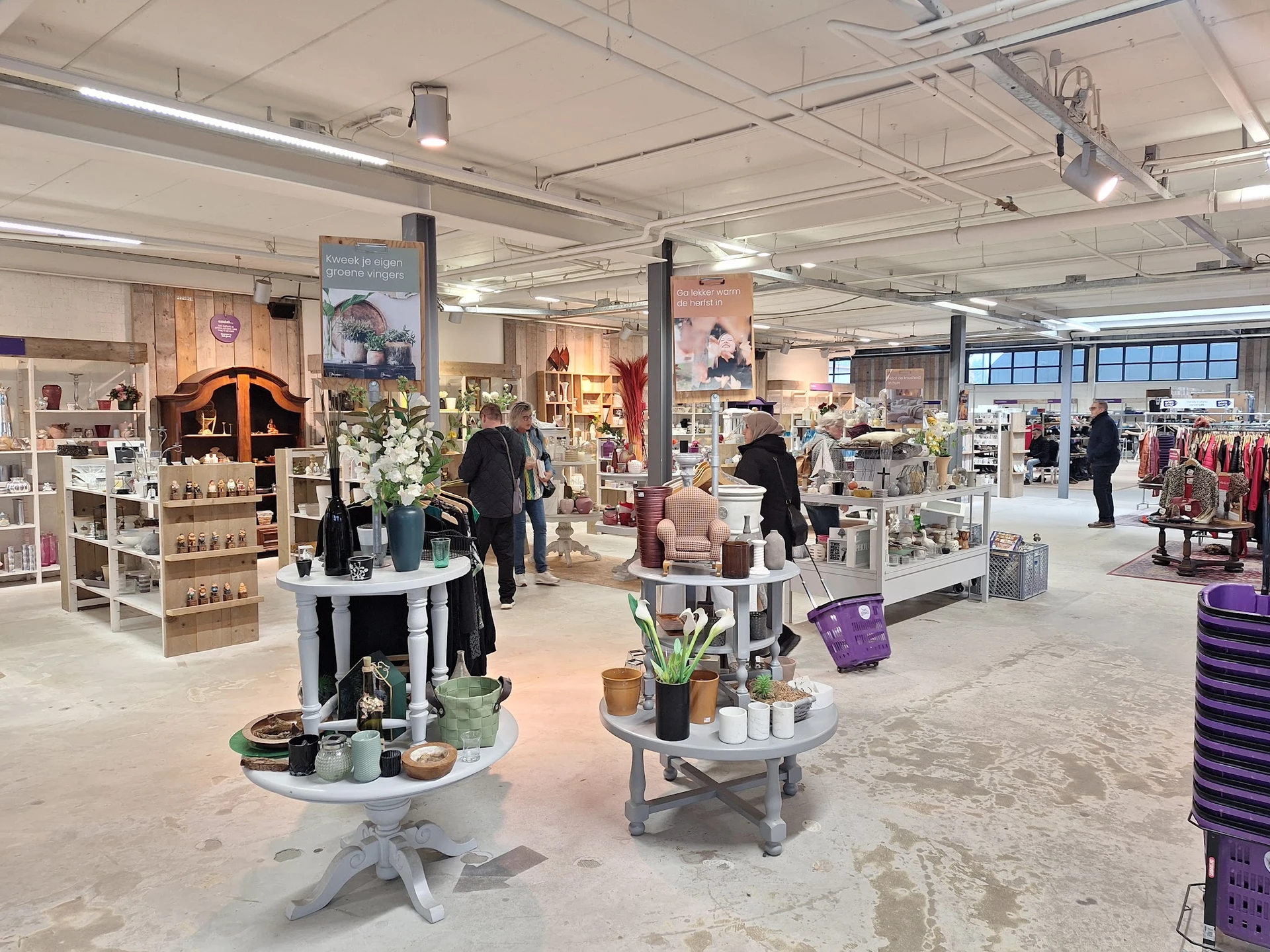 Ruim winkelinterieur met diverse afdeling, displaytafels met huishoudartikelen, klanten aan het winkelen, goed verlicht