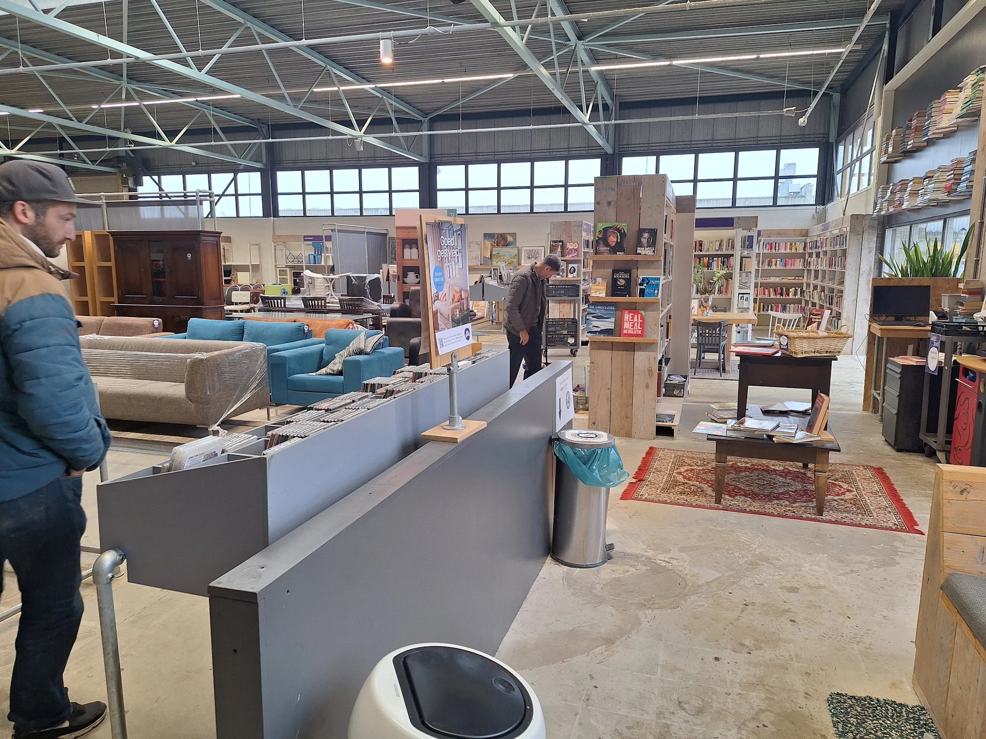 Winkelvloer van kringloopwinkel met toonbank, blauwe meubels, boekenkasten en diverse spullen
