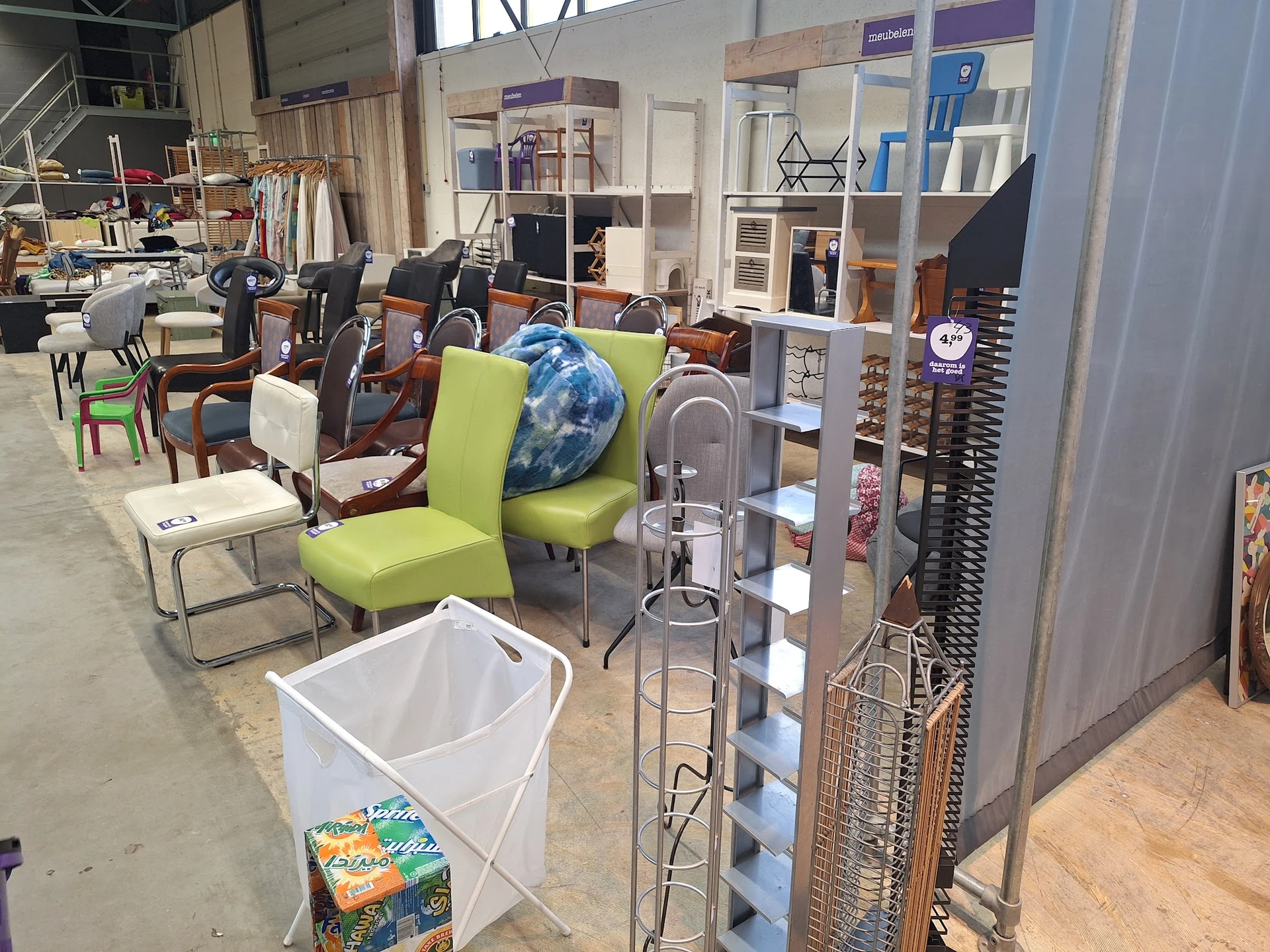 Winkelvloer met diverse meubels, stoelen en huishoudelijke spullen, stellingen met opbergdozen en een witte afvalbak