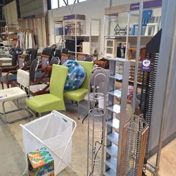 Winkelvloer met diverse meubels, stoelen en huishoudelijke spullen, stellingen met opbergdozen en een witte afvalbak