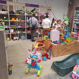 Speelgoedafdeling in kringloopwinkel met speelgoed uitgestald op houten display en stellingen met twee medewerkers in het mid
