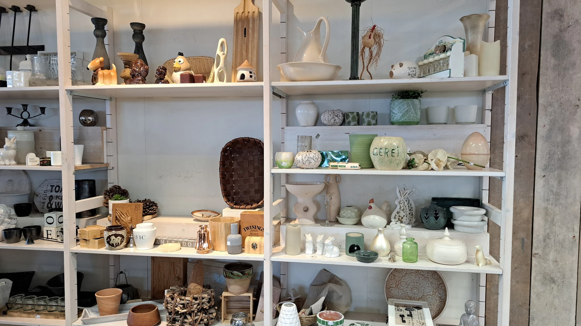 Witte stellingen vol huishoudelijke artikelen, decoratie en serviesgoed in de winkel