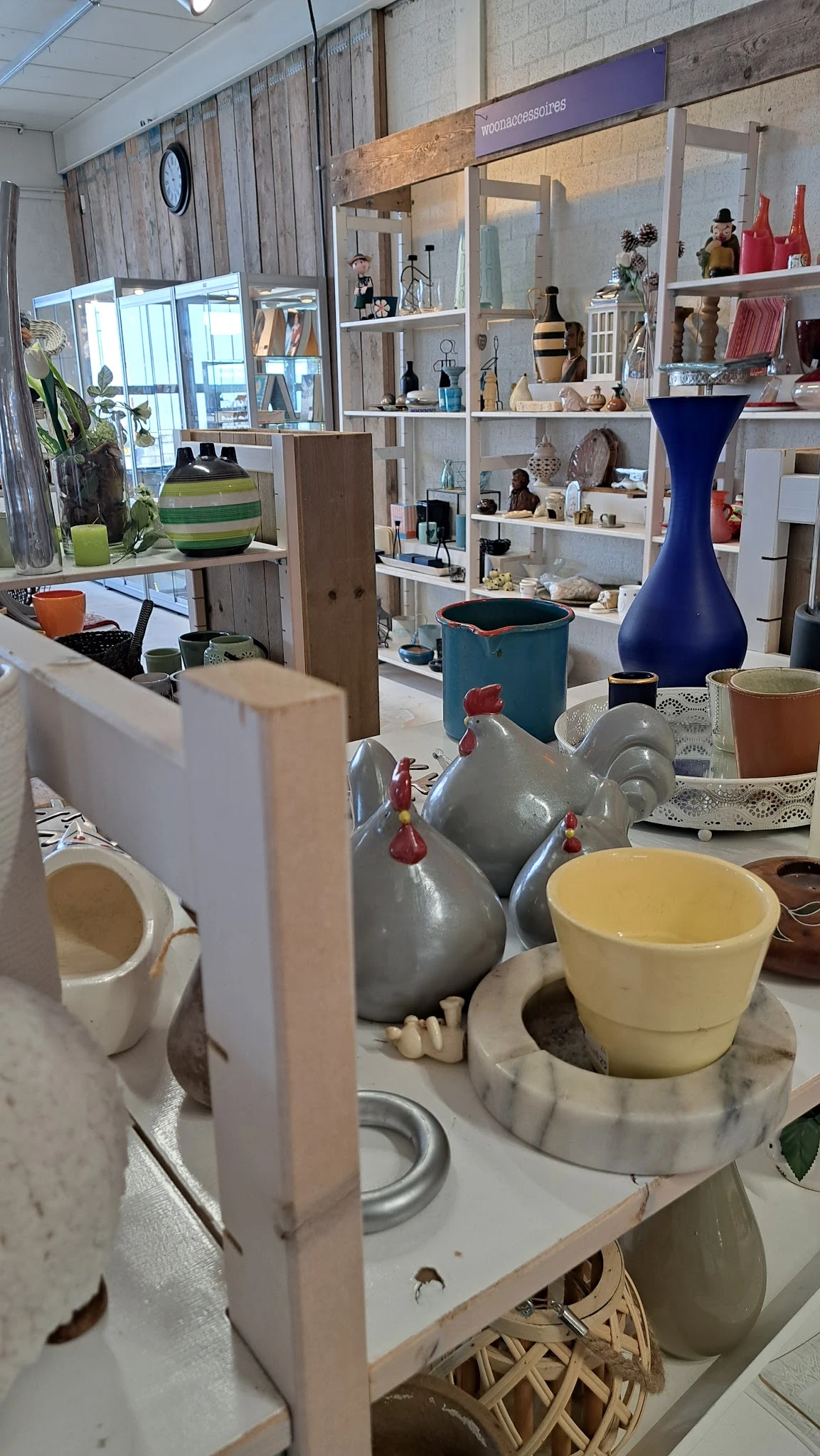 Diverse huishoudartikelen en serviesgoed uitgestald in een kringloopwinkel, waaronder grijze kannen, gele kom en blauwe vaas