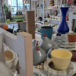 Diverse huishoudartikelen en serviesgoed uitgestald in een kringloopwinkel, waaronder grijze kannen, gele kom en blauwe vaas
