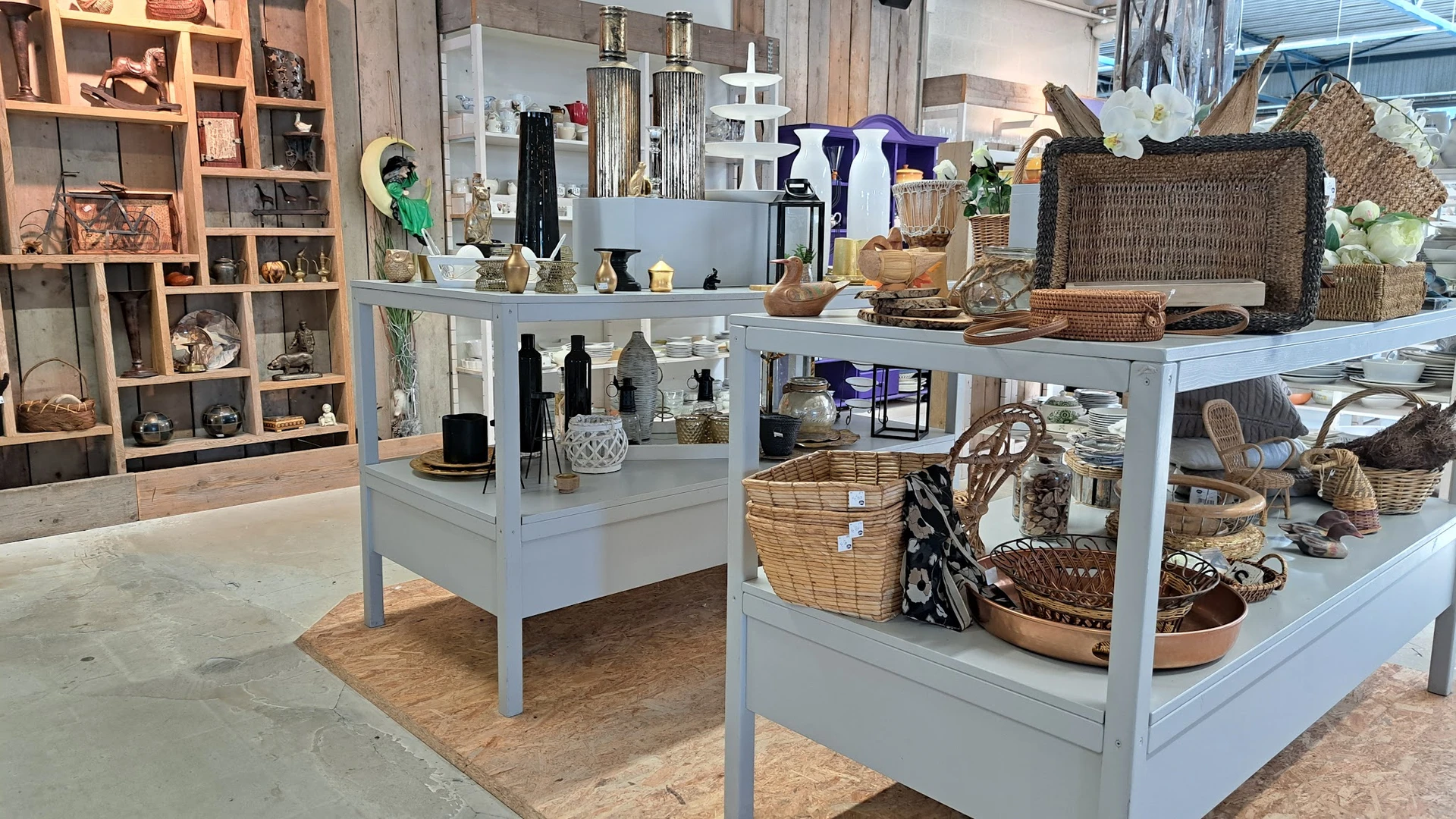 Lichte stellingen met decoratieve artikelen, huishoudelijke spullen en rieten manden in een kringloopwinkel