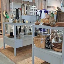 Lichte stellingen met decoratieve artikelen, huishoudelijke spullen en rieten manden in een kringloopwinkel