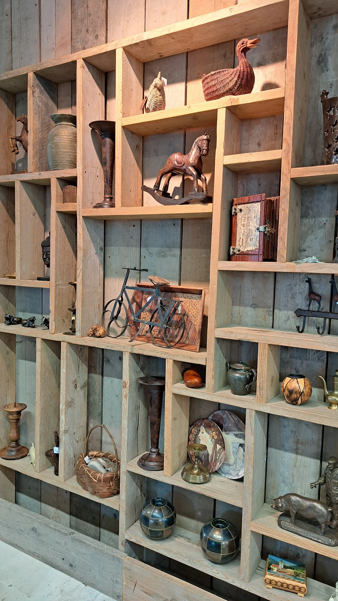 Houten stellingkast met tweedehands spullen: fiets, servies, lampen, boeken en decoratieartikelen