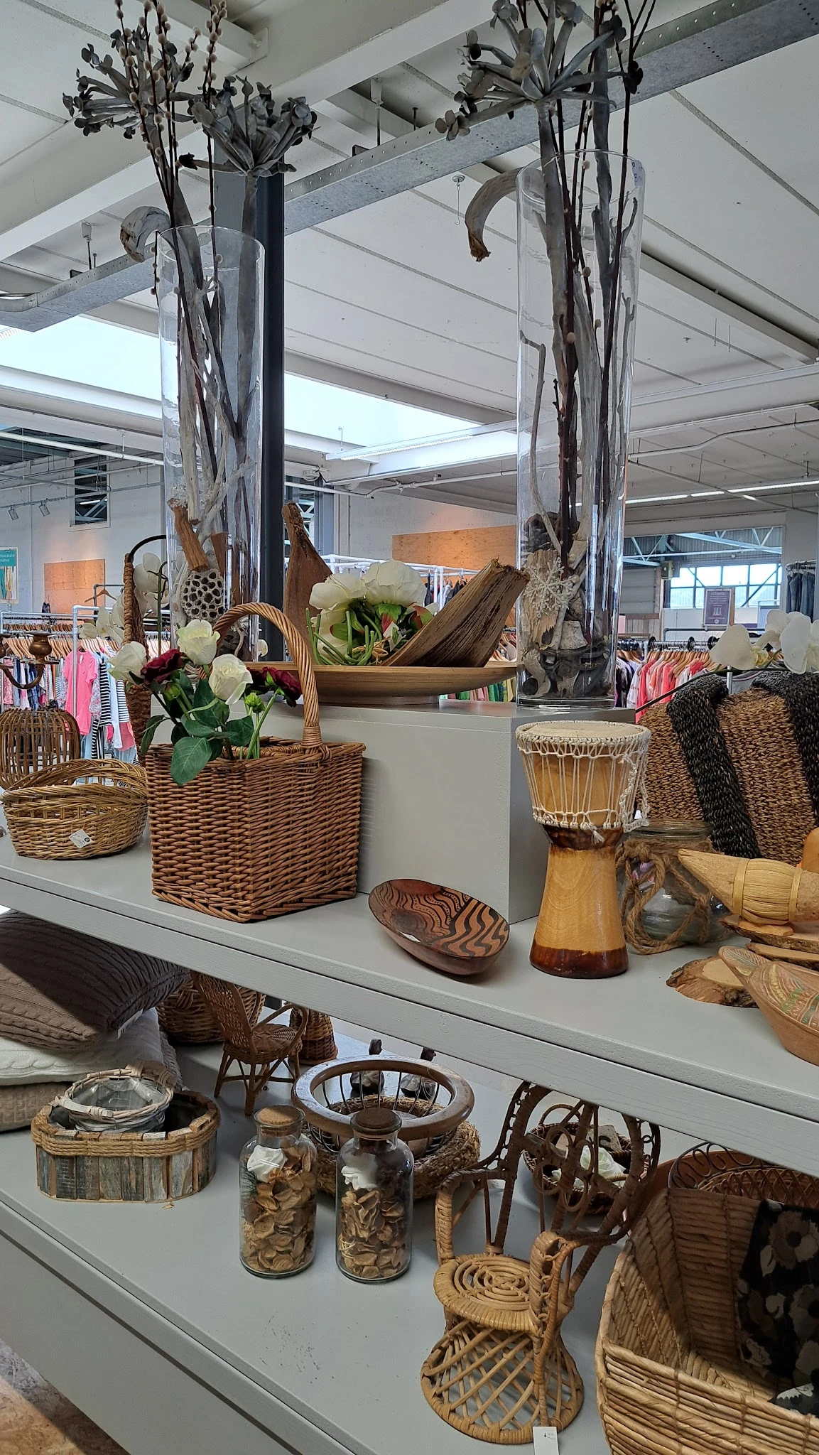 Uitgestalde decoratieve items: wikkelmanden met witte bloemen, houten schalen, trommels en textielwaren op een witte display.