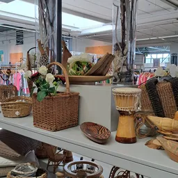 Uitgestalde decoratieve items: wikkelmanden met witte bloemen, houten schalen, trommels en textielwaren op een witte display.