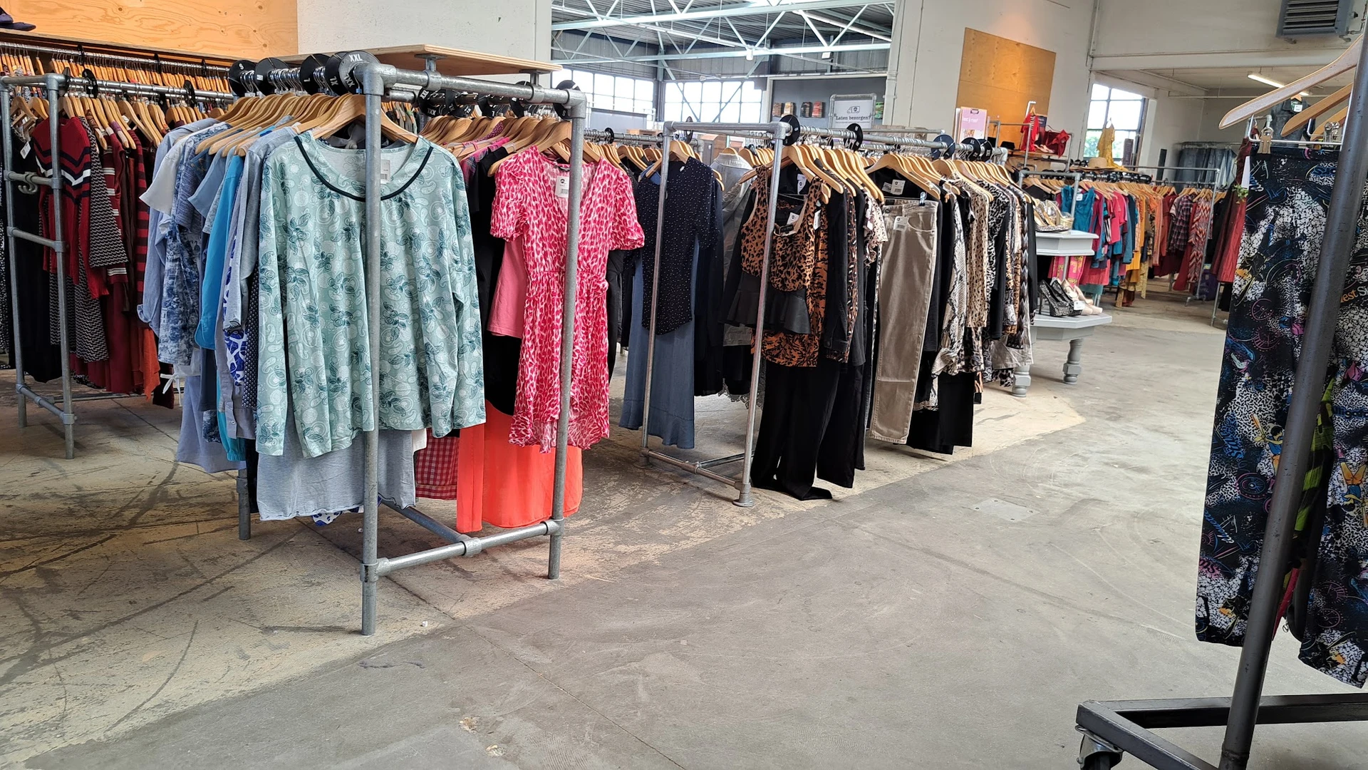 Rekken met tweedehands dameskleding in diverse kleuren en patronen in de winkel